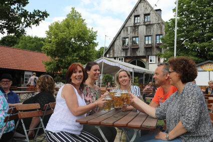 Gruppe sitzt im Biergarten am Seekrug und stößt mit einem Bier an