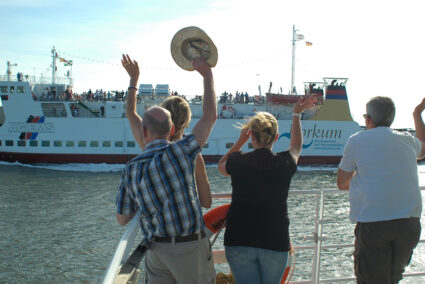 Menschen am Hafen in Borkum winken einer ankommenden Fähre