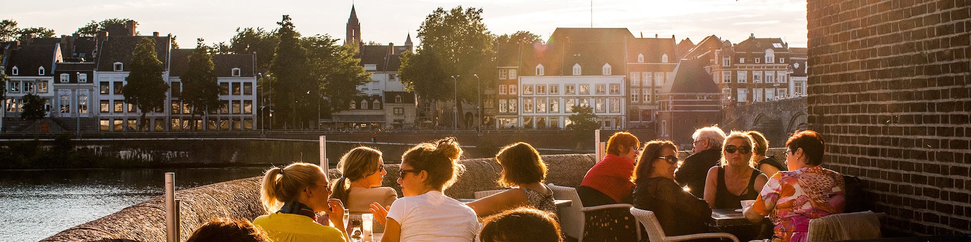 Menschen sitzen auf der Terasse vom Café Maas in Maastricht bei Sonnenuntergang