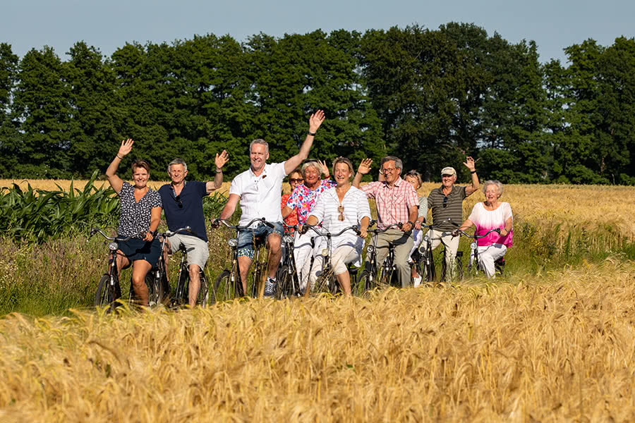 Eine Gruppe macht eine Radtour und fährt dabei auf einem Weg zwischen zwei Getreidefeldern