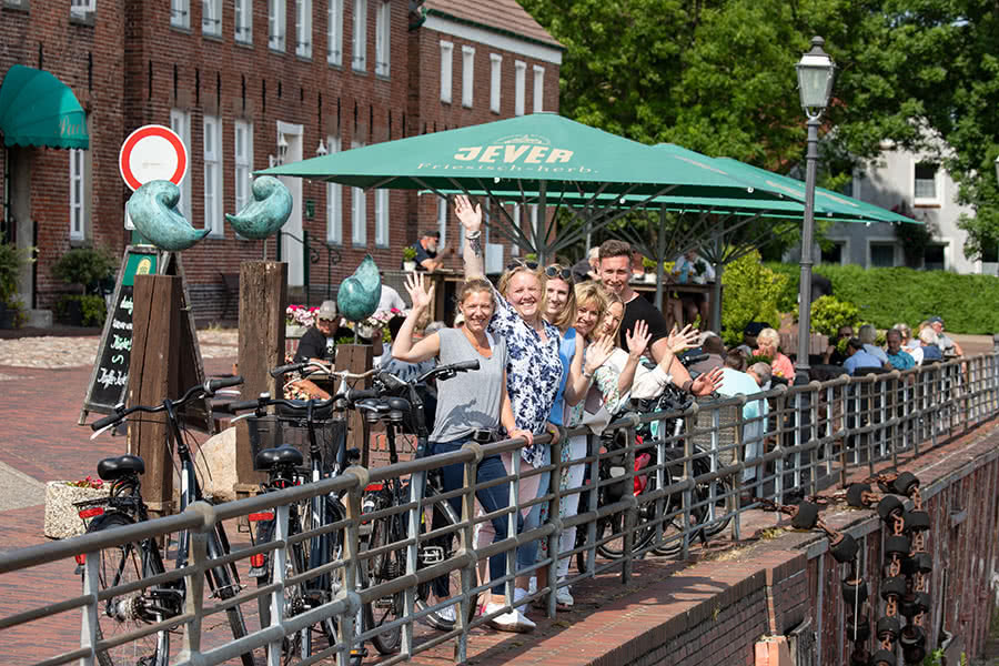 Eine Gruppe von 6 Personen steht an einem Geländer am Hafen und winkt